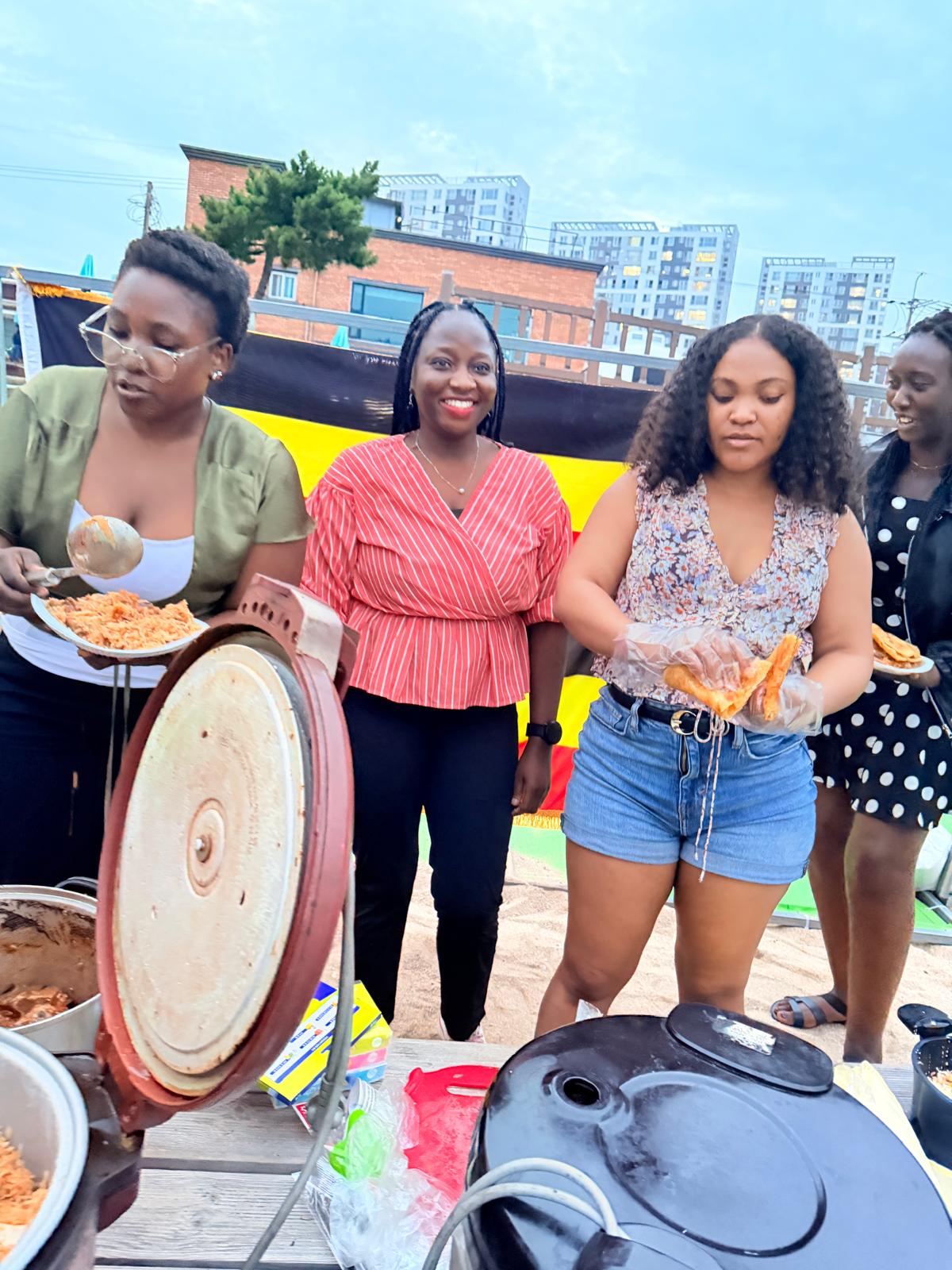 Members serving chapati and rice in front of the Uganda flag at the USKA food table on Bongpo Beach