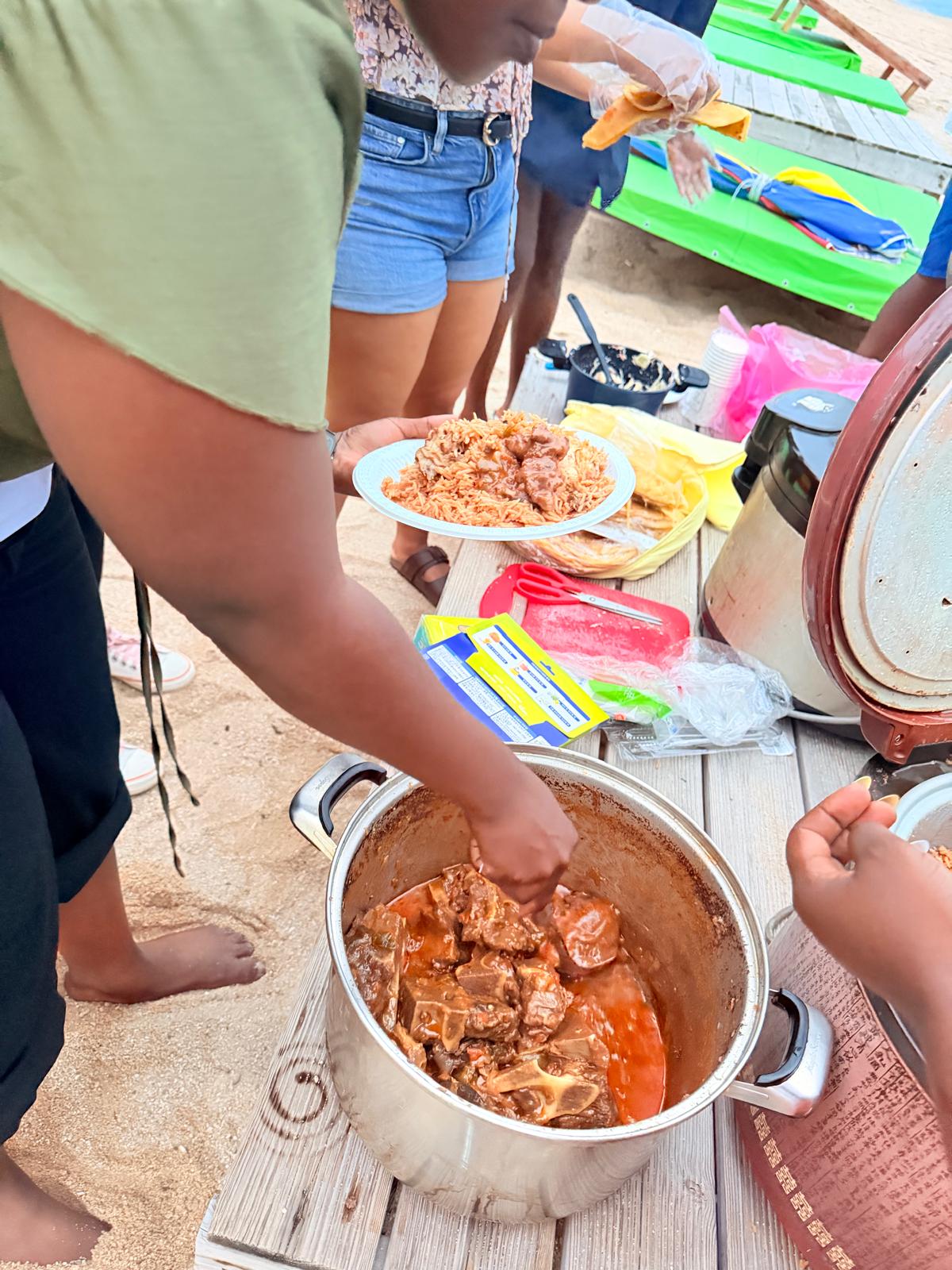 Stew being served from a pot onto a plate of rice at the USKA beach table, 15 August 2026